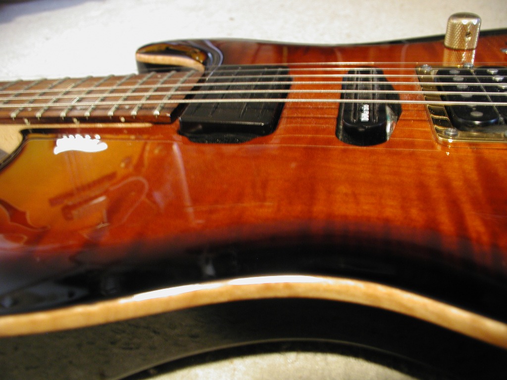 Close-up of an electric guitar neck and body in sunburst finish with pickups and strings